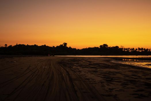 A beach with motorbike tracks in the sand during low tide and a bright orange sunset, peace and quiet, near Ngwesaung, Irrawaddy, western Myanmar