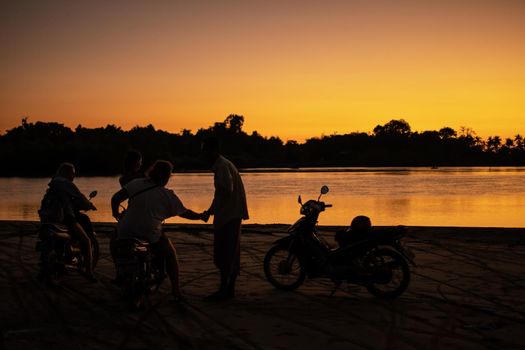 Ngwesaung, Myanmar - December 26, 2019: Four people with motorbikes on a beach watches the warm bright orange sunset on December 26, 2019 in Ngwesaung, Myanmar