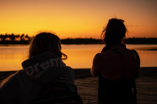 Two female friends on a sand beach watches the bright orange sunset near Ngwesaung, Irrawaddy, western, Myanmar