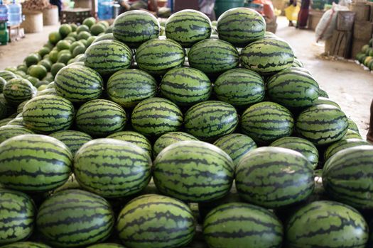 Many big and fresh watermelons stacked in a huge tower at a local street market in Myanmar