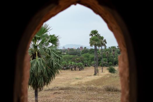 BAGAN, NYAUNG-U, MYANMAR - 2 JANUARY 2020: View from inside a pagoda over a few historical temples, a field and a forest