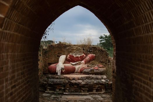 View of an old and historical broken buddha statue in red from an arched brick tunnel by a temple in Bagan, Myanmar