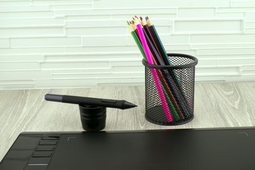 Digital stylus pen near digital graphic tablet for illustrators and designers opposite colored drawing pencils. Free space for text