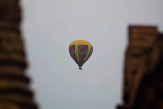 BAGAN, NYAUNG-U, MYANMAR - 2 JANUARY 2020: A yellow, green, red and blue multicolored hot air balloon in the sky above a historic temple