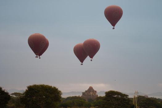 BAGAN, NYAUNG-U, MYANMAR - 2 JANUARY 2020: A few hot air balloons rises above a historic pagoda temple in the distance