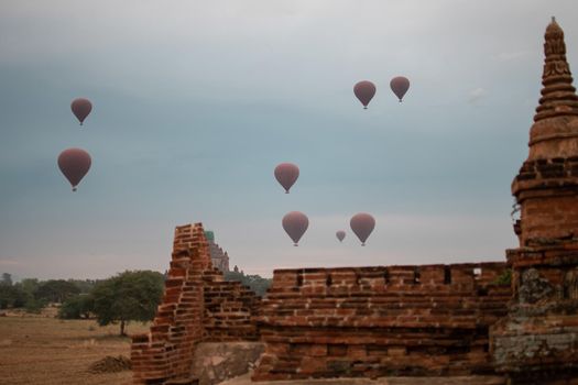 BAGAN, NYAUNG-U, MYANMAR - 2 JANUARY 2020: A few hot air balloons rises above a historic pagoda temple in the distance