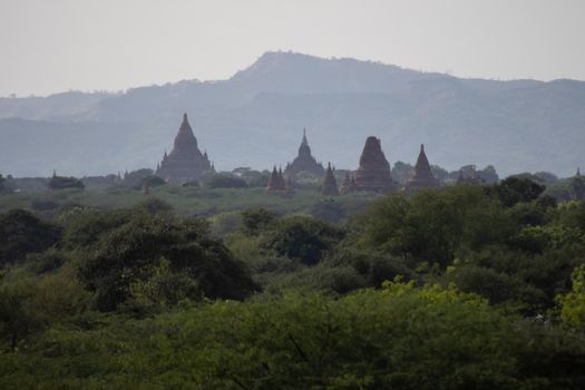 BAGAN, NYAUNG-U, MYANMAR - 3 JANUARY 2020: The top of old and historical temples peaking out above the tree vegetation in the distance
