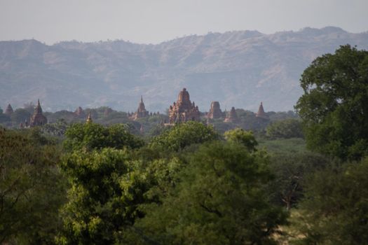 BAGAN, NYAUNG-U, MYANMAR - 3 JANUARY 2020: The top of old and historical temples peaking out above the tree vegetation in the distance