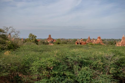 BAGAN, NYAUNG-U, MYANMAR - 3 JANUARY 2020: The top of old and historical temples peaking out above the tree vegetation in the distance