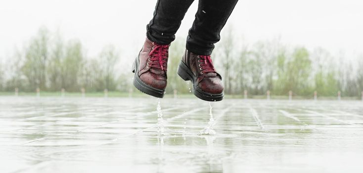 woman running on asphalt in rainy weather. Close up of legs and shoes splashing in puddles.