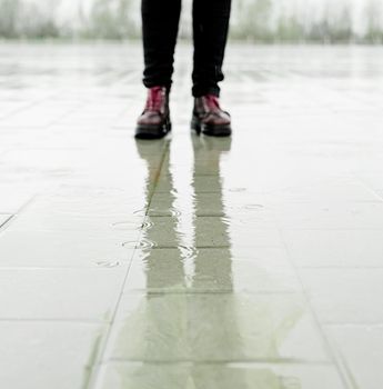 woman walking on asphalt in rainy weather. Close up of legs and shoes standing in puddles