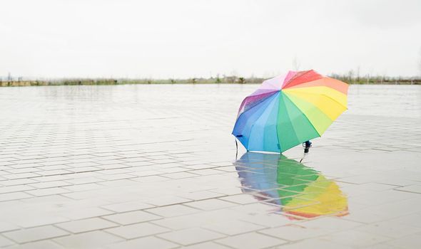 Unused colorful umbrella lying on ground being rained upon. Rainbow colored umbrella lying in puddles on the wet street ground. Copy space