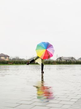 woman in yellow raincoat holding rainbow umbrella out in the rain