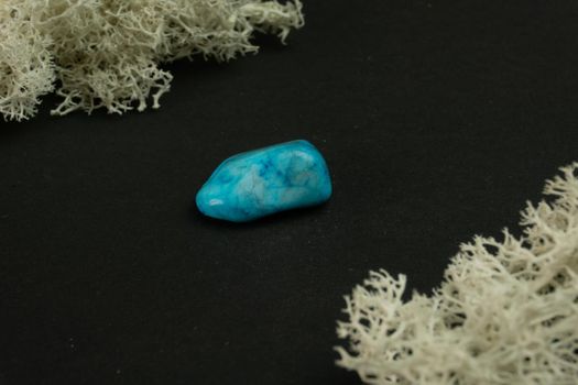 Howlite or turquoise imitation from Republic of South Africa RSA. Natural mineral stone on a black background surrounded by moss. Mineralogy, geology, magic, semi-precious stones and samples of minerals