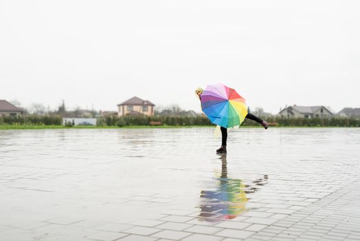 Beautiful brunette woman in yellow raincoat holding rainbow umbrella out in the rain