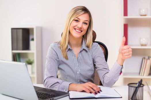 Beautiful businesswoman showing thumb up while  working at her office.