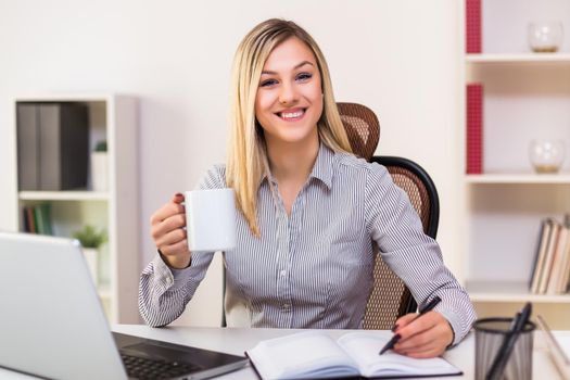 Businesswoman drinking coffee while working in her office.