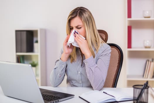 Businesswoman blowing nose while working in her office.
