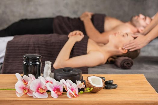 Beautiful couple relaxing together at spa centre at beauty treatment massage, orchid flowers coconut and stones