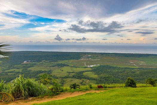 View from a large mountain to a valley with a lake in the Dominican Republic. Setting sun. Around greenery and red bushes