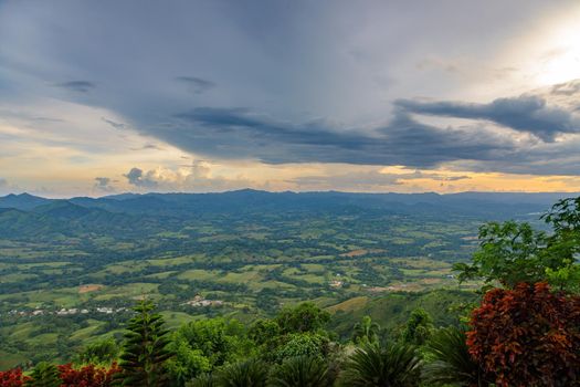 View from a large mountain to a valley with a lake in the Dominican Republic. Setting sun. Around greenery and red bushes