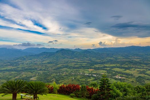 View from a large mountain to a valley with a lake in the Dominican Republic. Setting sun. Around greenery and red bushes