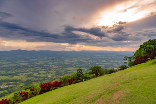 View from a large mountain to a valley with a lake in the Dominican Republic. Setting sun. Around greenery and red bushes