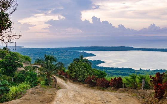 View from a large mountain to a valley with a lake in the Dominican Republic. Setting sun. Around greenery and red bushes