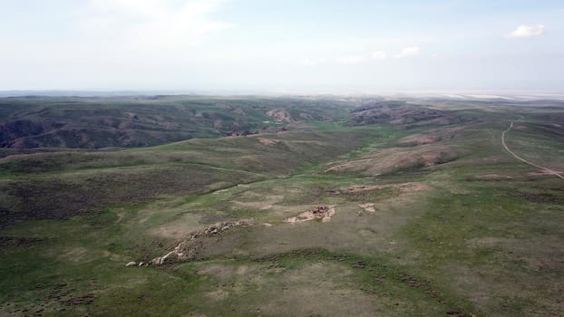 View of green hills and gorges with rocks. In the distance you can see the mountains, the river, the road. Hills covered with grass. Small gorges. Pure nature. Top view from the drone. Kazakhstan.