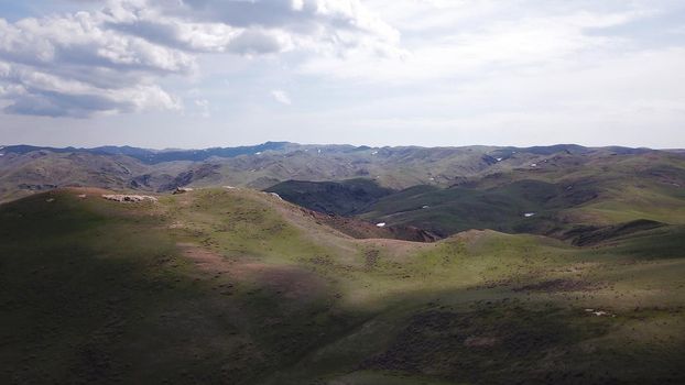 The shadow of the clouds runs over the green hills. In the distance you can see the mountains, the river, the road. Hills covered with grass. Small gorges. Pure nature. Top view from drone. Kazakhstan