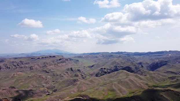 The shadow of the clouds runs over the green hills. In the distance you can see the mountains, the river, the road. Hills covered with grass. Small gorges. Pure nature. Top view from drone. Kazakhstan