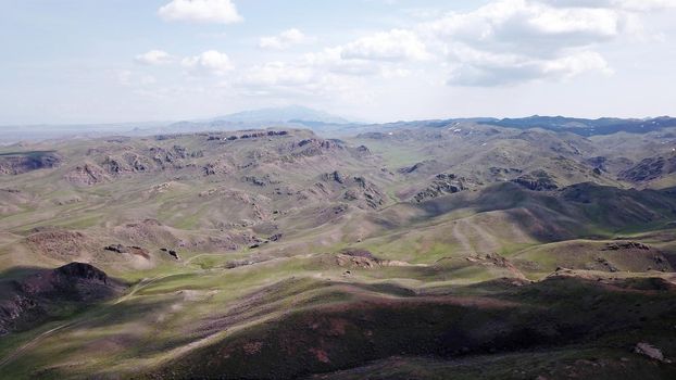 The shadow of the clouds runs over the green hills. In the distance you can see the mountains, the river, the road. Hills covered with grass. Small gorges. Pure nature. Top view from drone. Kazakhstan