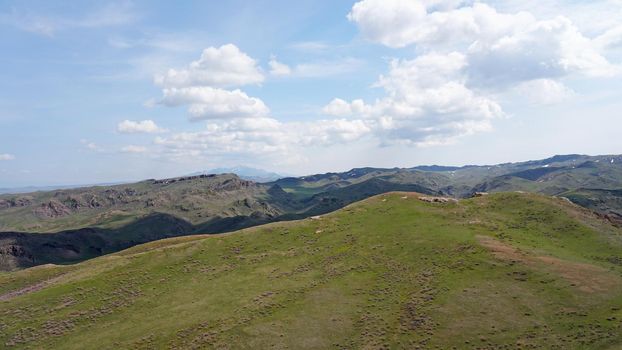 The shadow of the clouds runs over the green hills. In the distance you can see the mountains, the river, the road. Hills covered with grass. Small gorges. Pure nature. Top view from drone. Kazakhstan