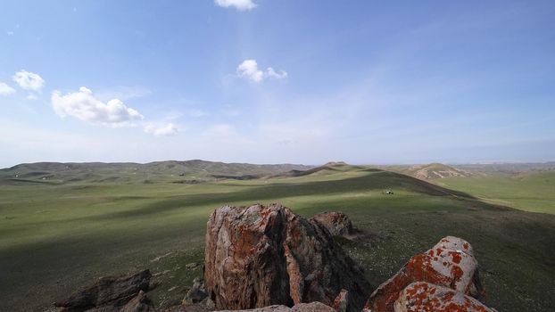 The shadow of the clouds runs over the green hills. In the distance you can see the mountains, the river, the road. Hills covered with grass. Small gorges. Pure nature. Top view from drone. Kazakhstan