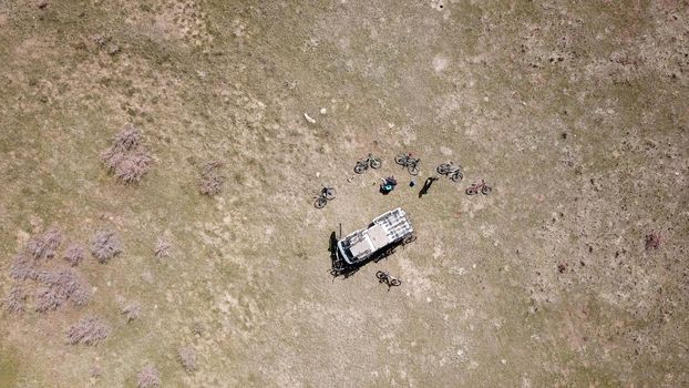 Car in the field with bicycles. Top view from the drone. Yellow-green field with bushes. Bicycles are lying around the car. Preparing for a trip to Kazakhstan. Yellow steppe.