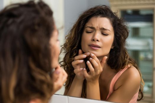 Beautiful woman squeezing pimple in the bathroom.