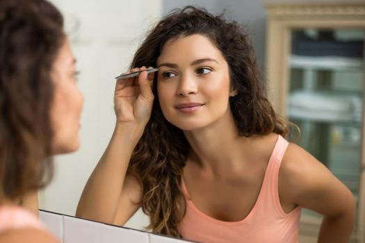 Beautiful woman plucking eyebrows in bathroom.