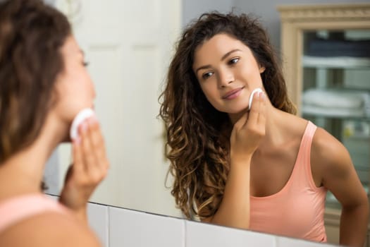 Beautiful woman cleaning her face with cotton pad in the bathroom.