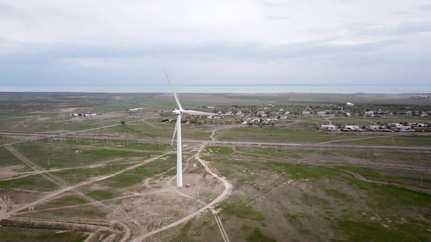 Windmills stand in the middle of green fields. Clean energy is generated. Cloudy weather, dark clouds. Green grass grows. High hills in the distance. Top view from drone. Industrial farm of Kazakhstan