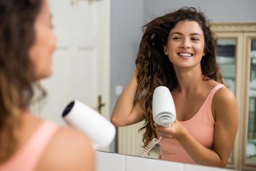 Young woman with gorgeous  curly hair using hairdryer.