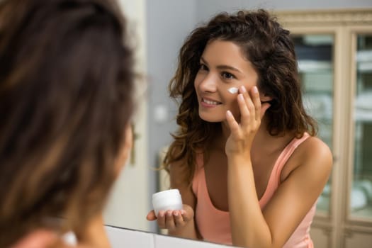 Beautiful woman applying moisturizer on her face.