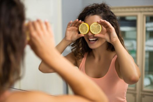 Beautiful woman is covering her eyes with slices of lemon in the bathroom.