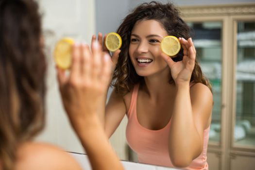 Beautiful woman holding  slices of lemon  in the bathroom.
