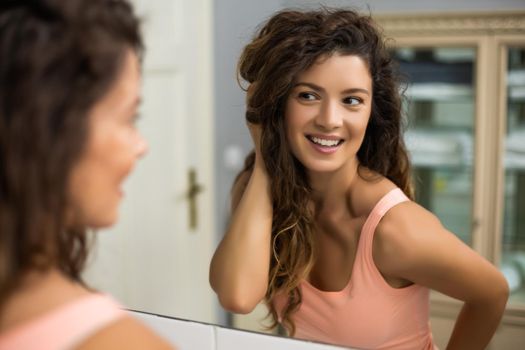 Beautiful woman with gorgeous long curly hair looking herself in the mirror.