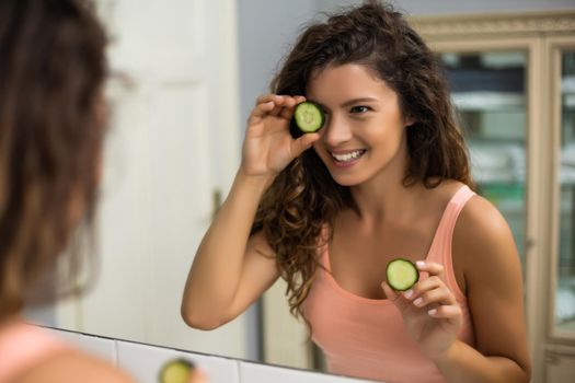 Beautiful woman holding  slices of  cucumber  in the bathroom.