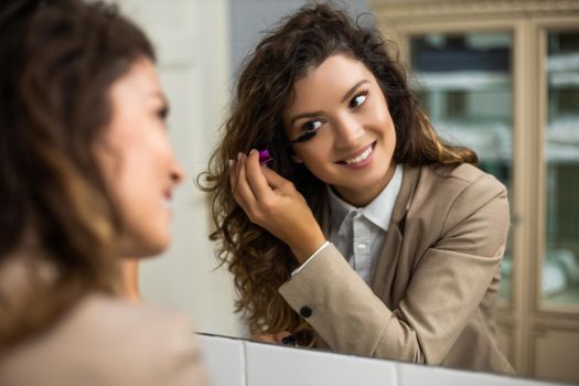 Businesswoman is applying mascara while preparing for work.