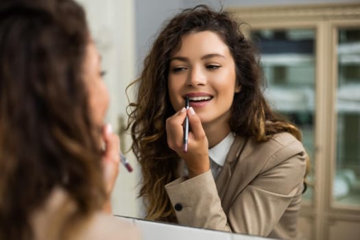 Businesswoman is applying  lipstick while preparing for work.