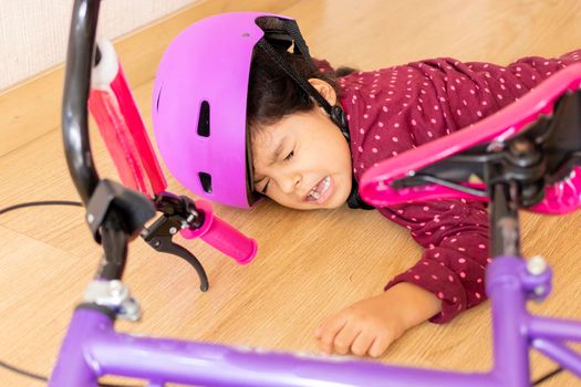 Sad little girl fell to the ground while playing with her bicycle in the house