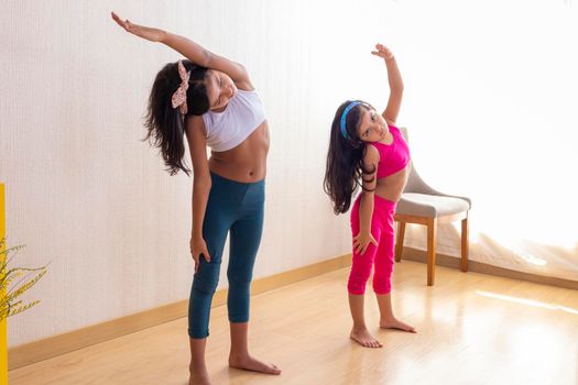 Two little sisters are doing exercise routines in the living room at home