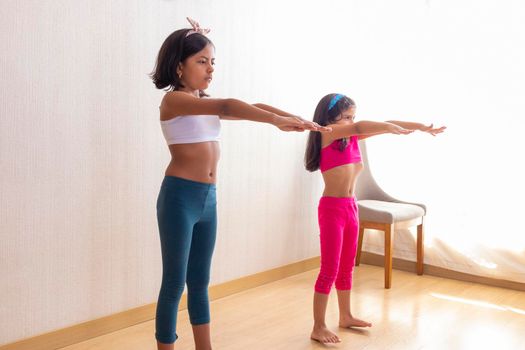 Two little sisters are doing exercise routines in the living room at home